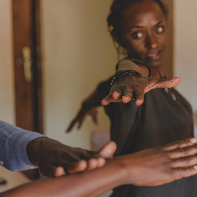 Talking through Art member Emilienne during a yoga class at TTA HQ in Kigali. The yoga class offers a change of pace for the members, from sitting and weaving or working in the kitchen, to exploring what their bodies can do alongside each other.